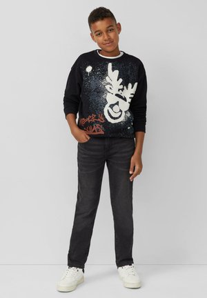 Schwarzer Sweatshirt mit einem Rentier-Graphic in Weiß und Spritzmuster, kombiniert mit schwarzen Jeans und weißen Sneakers. Lässiger Schnitt, lange Ärmel.