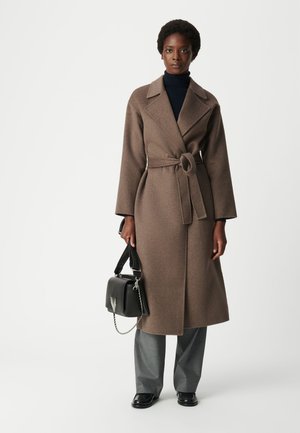 Bruine wollen trenchcoat met een ceintuur in de taille, met notch revers, lange mouwen en een middellange snit. Gepaard met grijze broek en een zwarte tas.