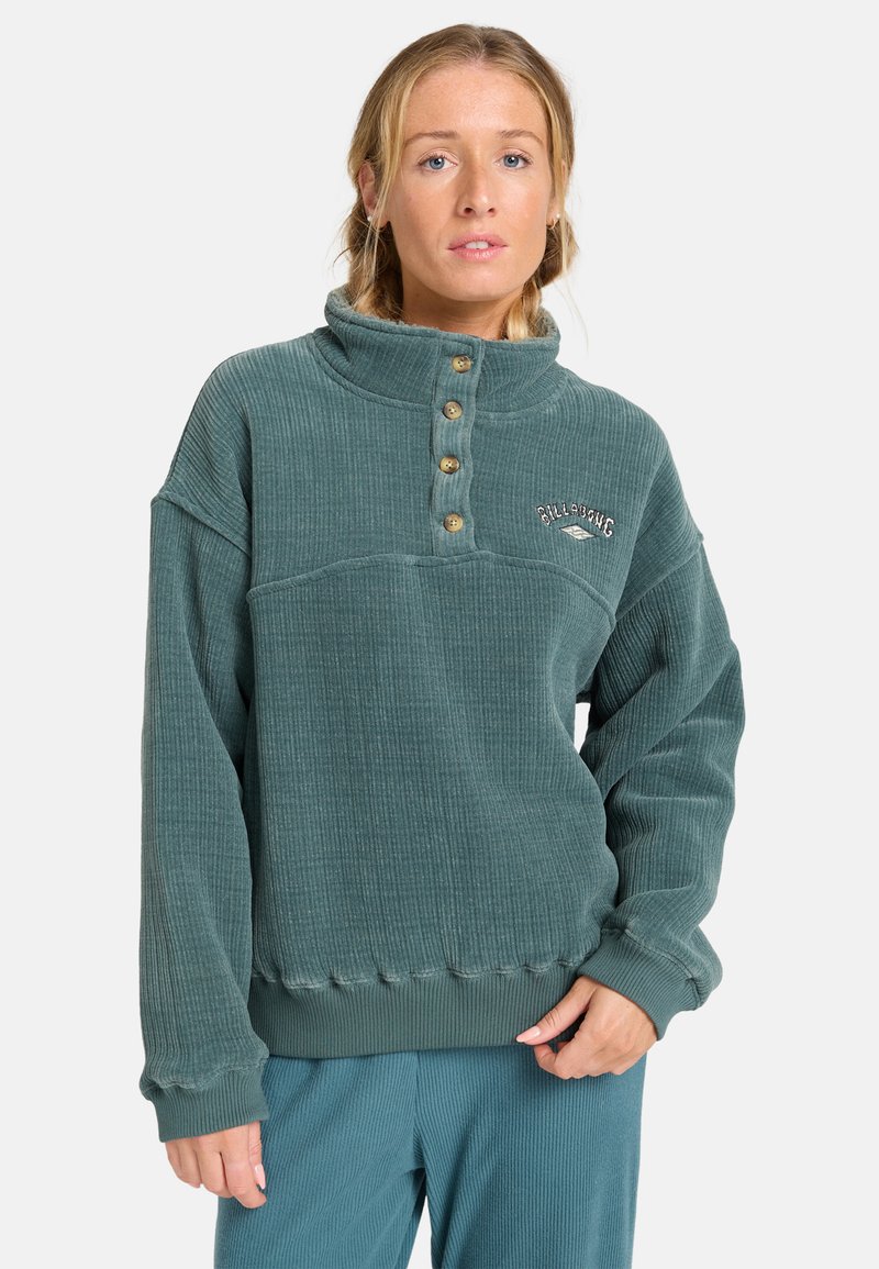 Suéter verde acanalado con cuello alto, cierre de botones en la parte delantera y logo bordado. Presenta un corte ligeramente oversize y una textura muy particular.