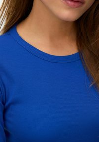 Dopasowany, niebieski top ze żłobieniami i okrągłym dekoltem, charakteryzujący się miękką teksturą i subtelnymi przeszyciami wzdłuż kołnierza.