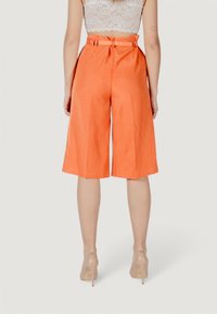 Culotte arancioni in lino con vita alta, pieghe frontali e tasche laterali. Combinati con un top in pizzo a bretelle e tacchi trasparenti.