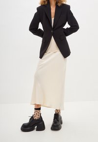 Black tailored blazer over a cream silk slip dress, paired with chunky black shoes and sheer, dotted socks. Minimalistic design, smooth textures.