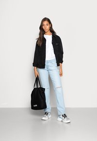 Casaco de ganga preto, t-shirt branca, jeans desalinhados de um azul claro, mala tote preta e ténis brancos largos com detalhes pretos.