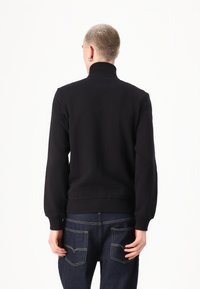 Sweatshirt preto de gola alta, com mangas longas e punhos canelados. Textura suave, usado com jeans azul escuro com dois bolsos traseiros.