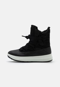 Botte noire imperméable présentant une tige en matériaux mixtes avec une finition semblable à du daim, une semelle intermédiaire blanche épaisse et une semelle extérieure en caoutchouc noir texturé.