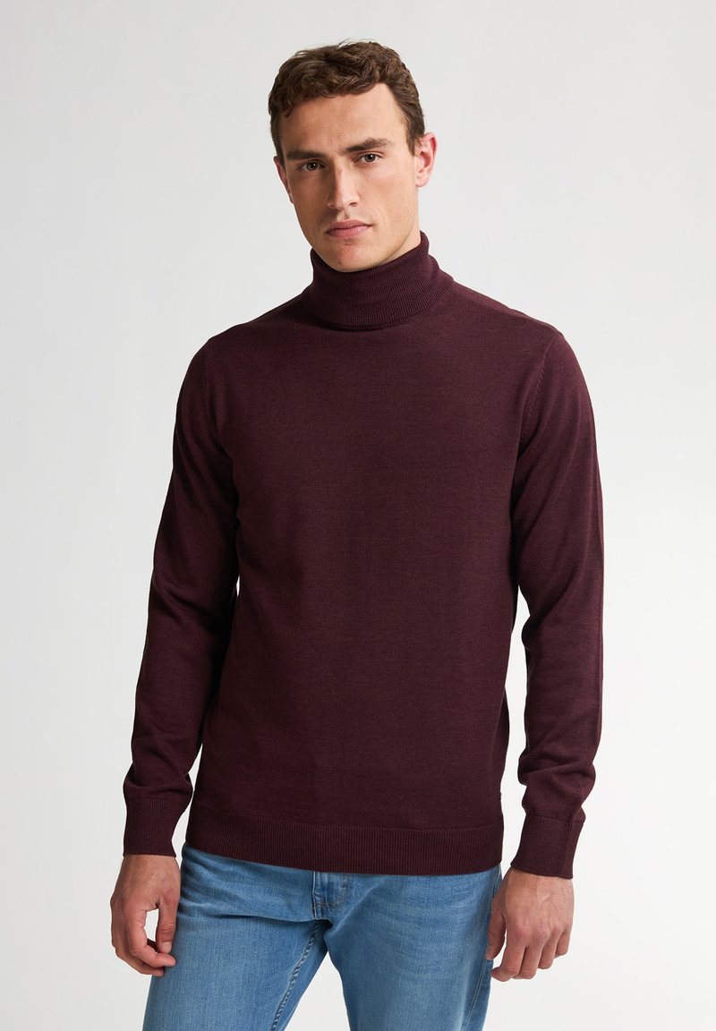 Burgunderfarbener Rollkragenpullover in figurbetontem Design mit geripptem Kragen und Bündchen, kombiniert mit hellblauen Jeans. Weiche Strickstruktur.