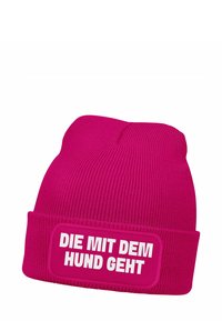 Pink knitted beanie with a ribbed texture and a folded cuff. It features a white rectangular patch with text: "DIE MIT DEM HUND GEHT."