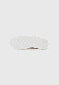 Hvit sneakersåle med et teksturert gummidesign, med riller og mønstrede grep for bedre feste. Merkevaren er preget på overflaten.