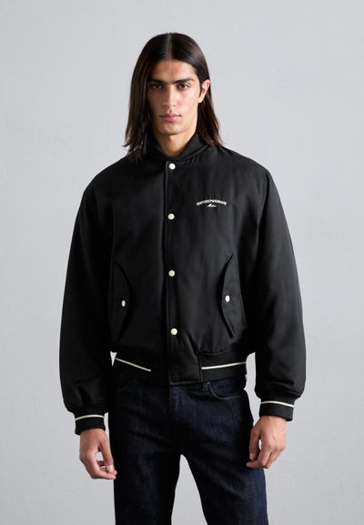 Schwarze Bomberjacke mit Druckknöpfen, gerippten Bündchen und weißen Akzenten. Verfügt über schräg eingeschnittene Taschen und ein gesticktes Logo auf der Brust.