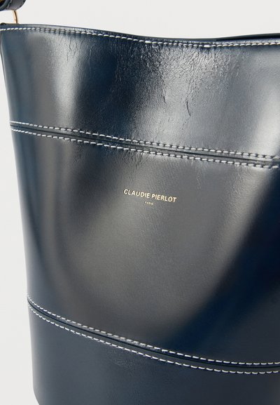 Λείο δερμάτινο τσάντα ώμου σε σκούρο μπλε χρώμα με λευκές ραφές και μικρό χρυσό λογότυπο "Claudie Pierlot Paris" στο κέντρο της μπροστινής πλευράς.