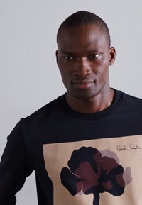 Schwarzer Sweatshirt mit einem großen abstrakten Blumenmotiv in Burgunder- und Rosatönen. Mit "Paul Smith"-Unterschrift in der Ecke.