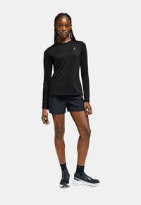 Black long-sleeve athletic top with a round neckline, paired with black shorts. Features lightweight fabric and a fitted design.