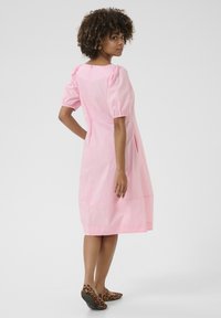 Roza obleka s puhastimi rokavi iz lahkega materiala, do kolen, s kvadratnim hrbtom in stranskimi žepi. Nosi se z balerinkami s tigrastim vzorcem.