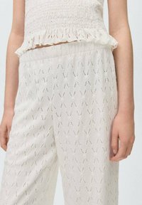 Witte gesmokte crop top met een gerimpelde zoom en wijde broeken met een gestructureerd patroon van diamantvormen en verticale lijnen.