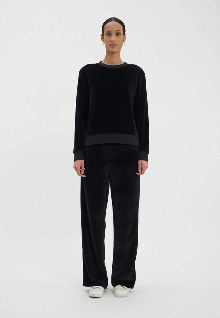 Ensemble coordonné en velours noir, comprenant un haut à manches longues avec un col rond et un pantalon à jambes larges. Le tissu a une texture douce et pelucheuse.