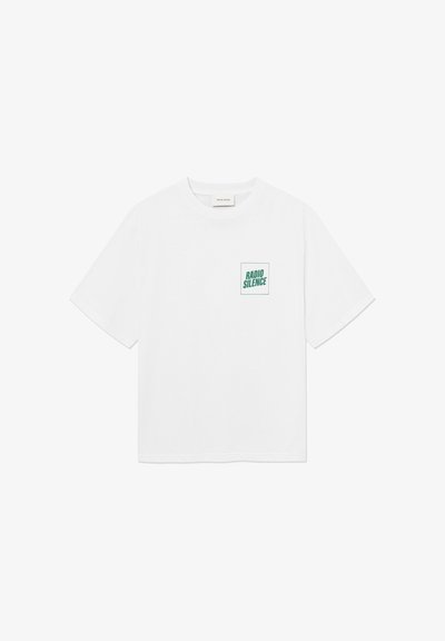 T-shirt blanc à manches courtes avec un petit texte vert "RADIO SILENCE" à l'intérieur d'un carré sur la partie supérieure gauche de la poitrine.
