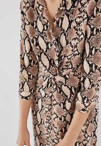 Abito a maniche lunghe con stampa a serpente in tonalità beige e nere. Realizzato in un tessuto testurizzato con dettagli a bottoni.