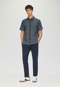 Korte mouwen navy geblokte shirt, katoenmix, knoopsluiting aan de voorkant, gecombineerd met donkere broek en witte sneakers met zwarte accenten.