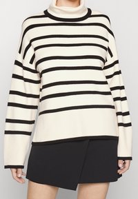 Sweter z golfem w kolorze kremowym w czarne poziome paski, z szerokimi, oversize'owymi rękawami i luźnym fasonem. Miękka włóknina.