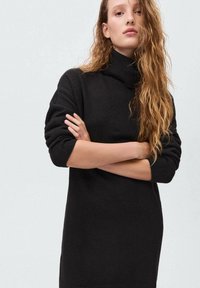 Černý rolák, pletená textura, dlouhé rukávy, uvolněný střih, obsahuje žebrované manžety a lem, minimalistický design.