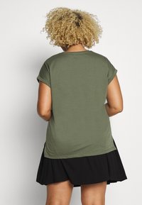 Olijfgroene t-shirt met korte mouwen en opgerolde mouwen, zachte textuur, gecombineerd met een zwarte geplooide rok, die een relaxte pasvorm en casual stijl laat zien.