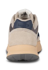 Beige suede tenisice s mornarsko plavim akcentima, teksturiranim petnim dijelom i mrežastim jezikom. Imaju svijetlosmeđu potplat s sivim uzorkom za prianjanje.
