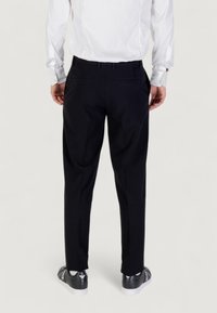 Pantaloni neri su misura con una texture liscia, pieghe frontali e tasche posteriori. Indossati con una camicia bianca e sneaker nere.