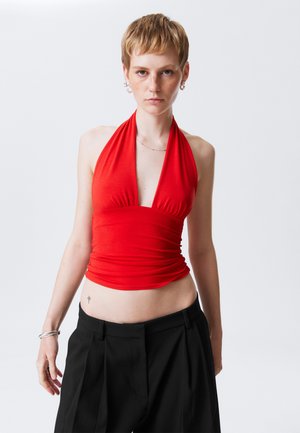 Sarkana halter top no stieptas auduma, ar dziļu V veida izgriezumu un sapulcētu detaļu jostā, apvienota ar augsto vidukļa melno biksēm.