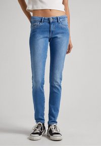 Blauwe skinny jeans van denim met een gemiddelde taillehoogte, voorzien van een klassieke vijf-pocketontwerp en subtiele vervaging. Gecombineerd met zwart-witte sneakers.