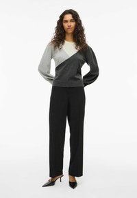 Pull color block gris et noir avec manches longues et col rond, associé à un pantalon noir taille haute et des escarpins noirs à bout pointu.