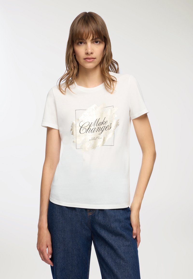 Biała bawełniana koszulka z krótkim rękawem, z nadrukiem ze złotej folii mówiącym "Wprowadzaj zmiany" na teksturowanym tle. Luźny krój, okrągły dekolt.