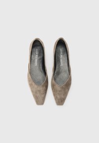 Des talons aiguilles en daim taupe, avec un design à découpe basse. L'intérieur est doublé d'un tissu sombre, mettant en valeur la texture de la chaussure.