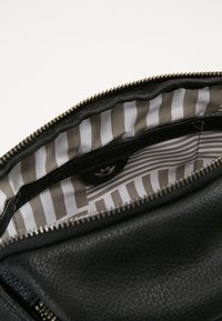 Mustalla nahkalaukulla, jossa on vetoketjukiinnitys ja raidallinen beige-valkoinen vuori sekä pieni tasku napsautettavalla napilla.