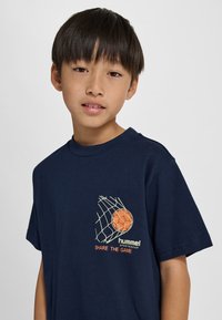 Navy katoenen t-shirt met een basketbalnetgrafiek met een oranje bal en "hummel"-logo. Met korte mouwen en een ronde halslijn.