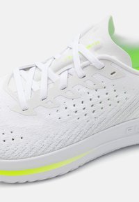Chaussure de sport avec une tige en maille blanche, des accents vert fluo et une semelle texturée. Présente des perforations pour la respirabilité et des lacets plats.