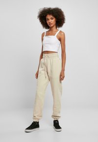 Bílý crop top s širokými ramínky a čtvercovým výstřihem, doplněný béžovými tepláky s elastickým pasem a šňůrkou. Černé tenisky.