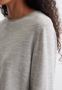 Pull gris clair à la texture lisse, col rond et manches longues. Le tissu semble doux et léger. Design minimaliste.