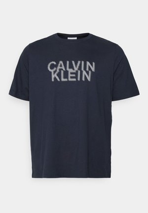 Camiseta de algodón azul marino con la inscripción "CALVIN KLEIN" en letras blancas punteadas. Cuello redondo clásico, mangas cortas y ajuste relajado.
