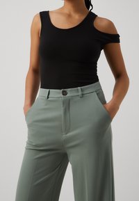 Czarny dopasowany top na ramiączkach z wycięciami na ramionach, w zestawieniu z jasnoszarymi spodniami o wysokim stanie, z guzikami z przodu i bocznymi kieszeniami.