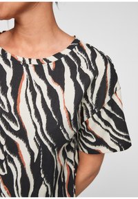 Top de manga corta en estampado de cebra en blanco y negro, con un acento naranja. Tejido suave con cuello redondo y corte relajado.