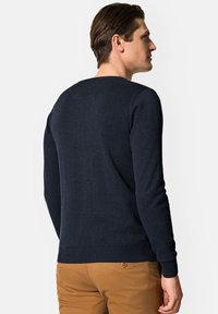 Granatowy sweter dzianinowy z okrągłym dekoltem i prążkowanymi mankietami, noszony z beżowymi spodniami; gładka tekstura, uniwersalny krój.