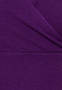 Närbild av texturerad lila stickad tyg med överlappande diagonala ribbade mönster och horisontell sömdetalj.