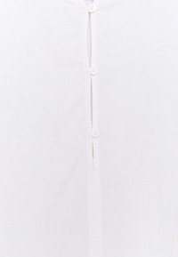 Camicia bianca in lino con patta di bottoni e cinque bottoni bianchi disposti verticalmente. Tessuto morbido e testurizzato con un design semplice e pulito.