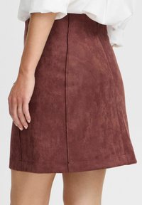 Burgunderfarbene Wildlederrock mit glatter Textur, tailliertem Schnitt und subtilen Nahtdetails, der über dem Knie endet und eine schlanke Silhouette schafft.