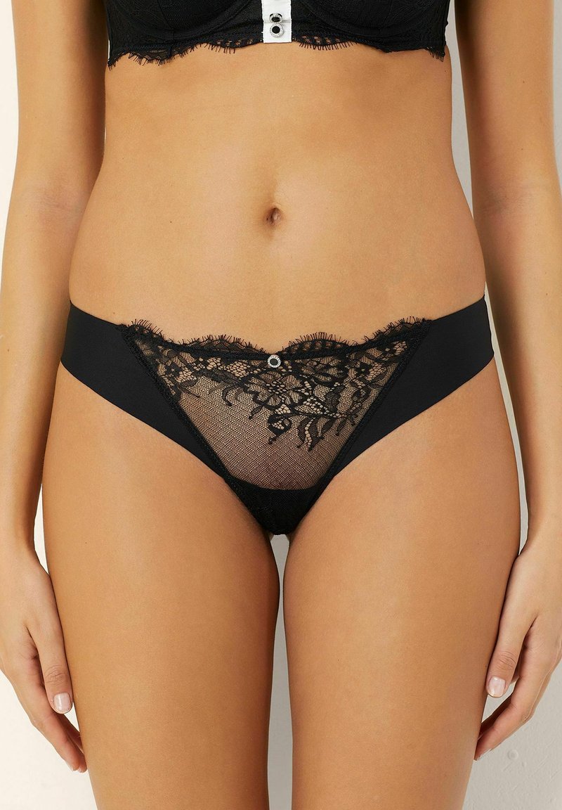 Czarne koronkowe majtki w bikini z prześwitującym siateczkowym przodem, falbaniastymi krawędziami i dekoracyjnym guzikiem na środku przodu.
