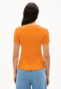 Oranje aansluitend t-shirt met korte mouwen, ribbelstructuur en een ronde halslijn, gecombineerd met lichtblauwe high-waisted spijkerbroek.