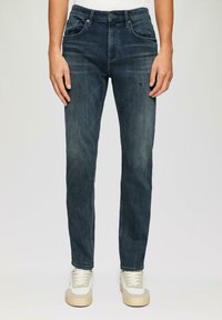 Jeans in denim blu scuro con una vestibilità slim, dotati di cinque tasche, leggero sbiadimento e un piccolo strappo consumato sulla parte anteriore della coscia sinistra.