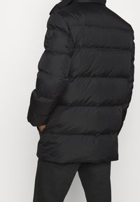 Sort puffjakke med en quiltet design, der har en høj krave og elastiske manchetter. Materialet virker glat og vandafvisende.