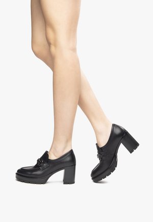 Scarpe nere in pelle con tacco, punta rotonda, una prominente fibbia decorativa e un tacco spesso texturizzato, che mostra una superficie liscia.