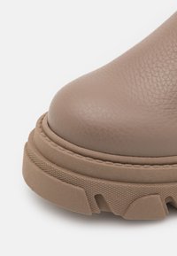 Botte de cheville en cuir marron avec un dessus texturé, un bout rond et une semelle en caoutchouc épaisse avec des rainures pour une meilleure adhérence.